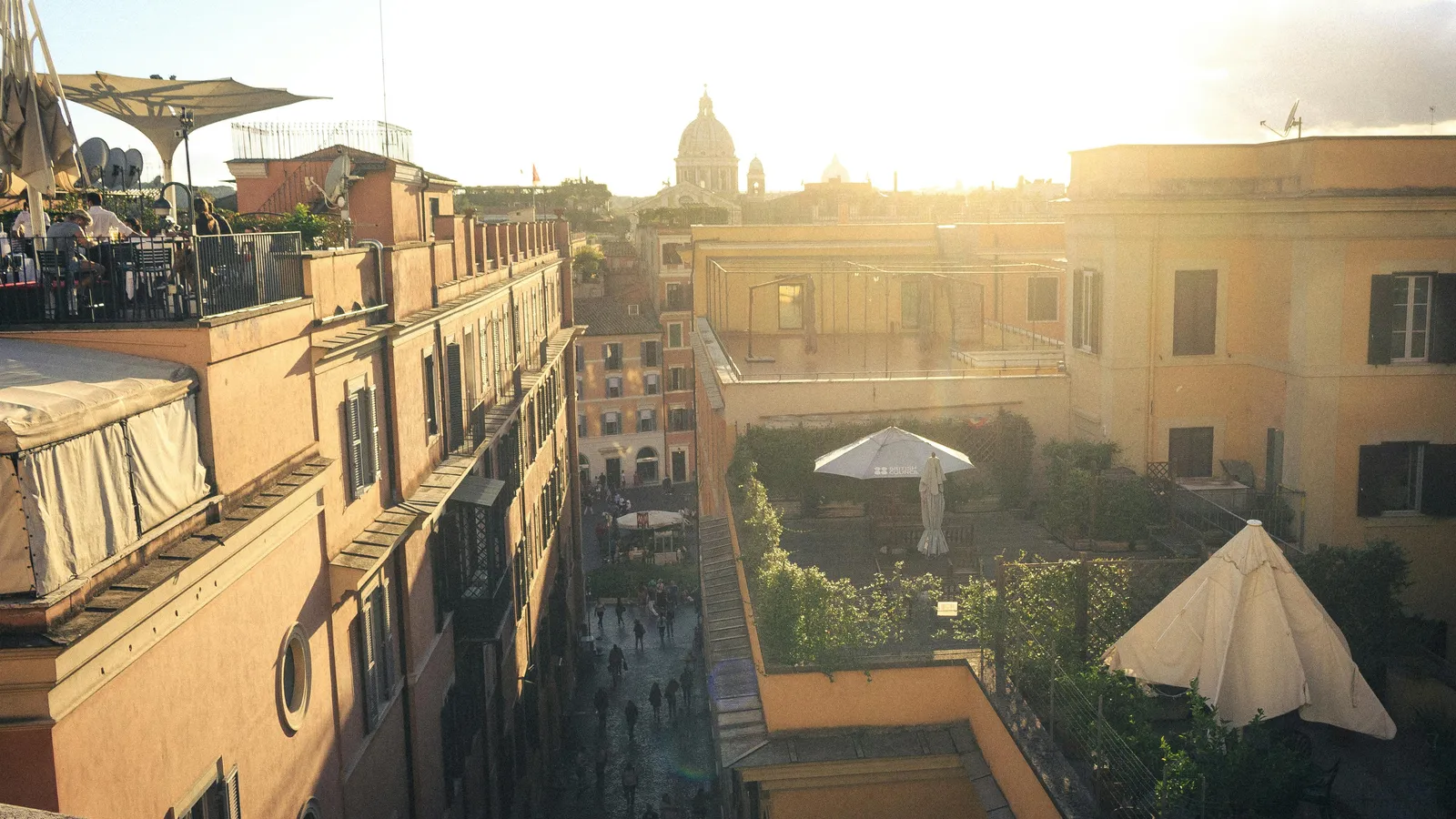 The rooftop terrace at Hotel Colle Oppio at golden hour, looking northwest over Monti rooftops toward Santa Maria Maggiore — the kind of quiet adult corner the post is about.
