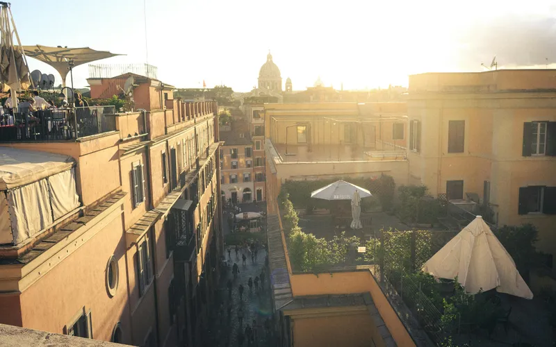 The rooftop terrace at Hotel Colle Oppio at golden hour, looking northwest over Monti rooftops toward Santa Maria Maggiore — the kind of quiet adult corner the post is about.
